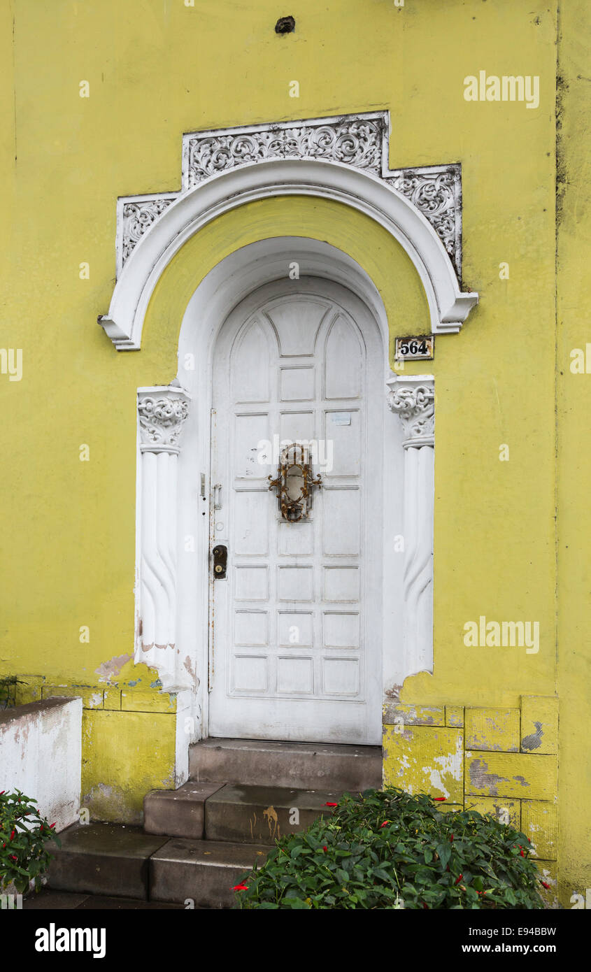 White door and stucco work with peeling paint in a yellow wall of a neglected suburban colonial house in the suburb of Miraflores, Lima, Peru Stock Photo