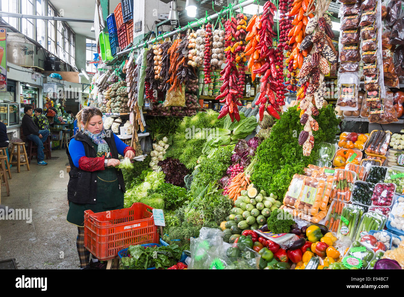 Local woman stallholder with typical colourful display of fresh peppers and vegetables at a stall at Surquillo Market, Miraflores, Lima, Peru Stock Photo