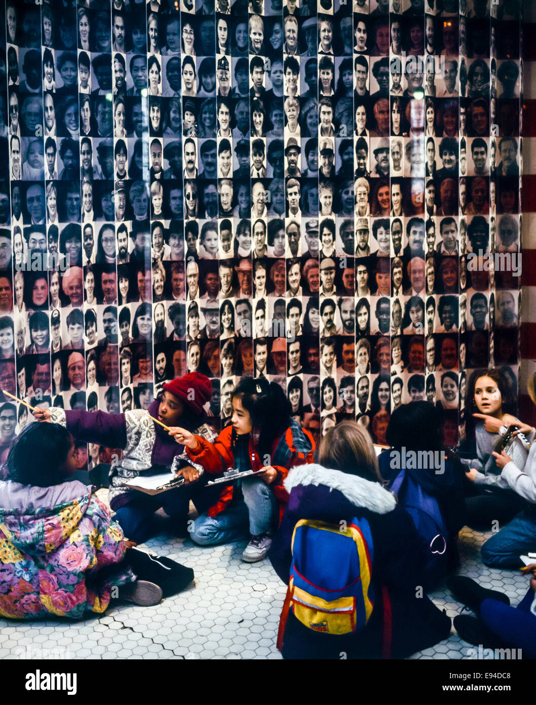 Schoolchildren visiting Ellis Island Immigration Museum, sitting in front of flag of faces, New York, NY, USA Stock Photo