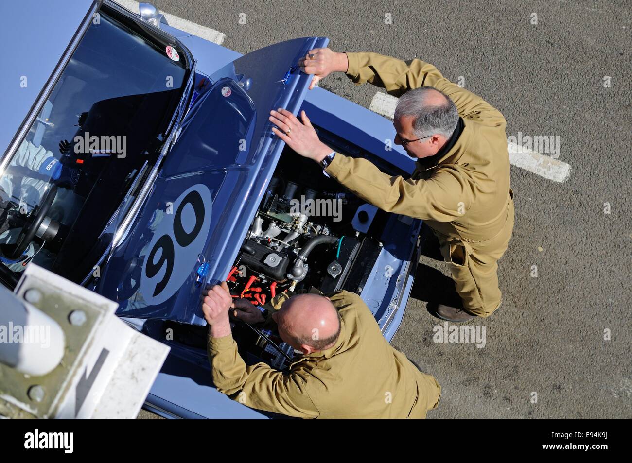 Overhead shot of two mechanics in the pit lane at Goodwood opening up the bonnet of a Fiat classic racing car. Stock Photo
