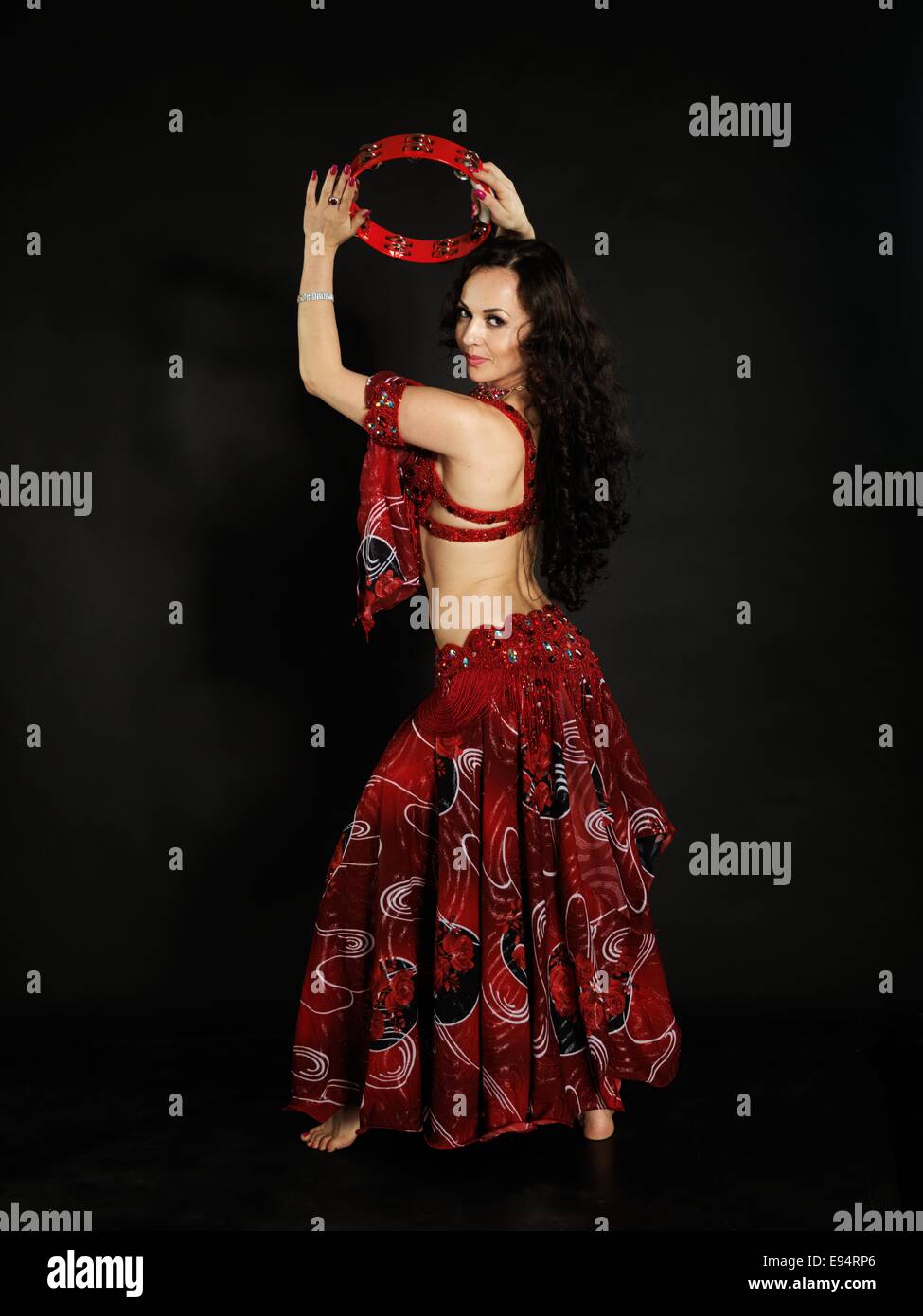 Young beautiful dancer with a tambourine wearing gypsy costume in front of the black back ground