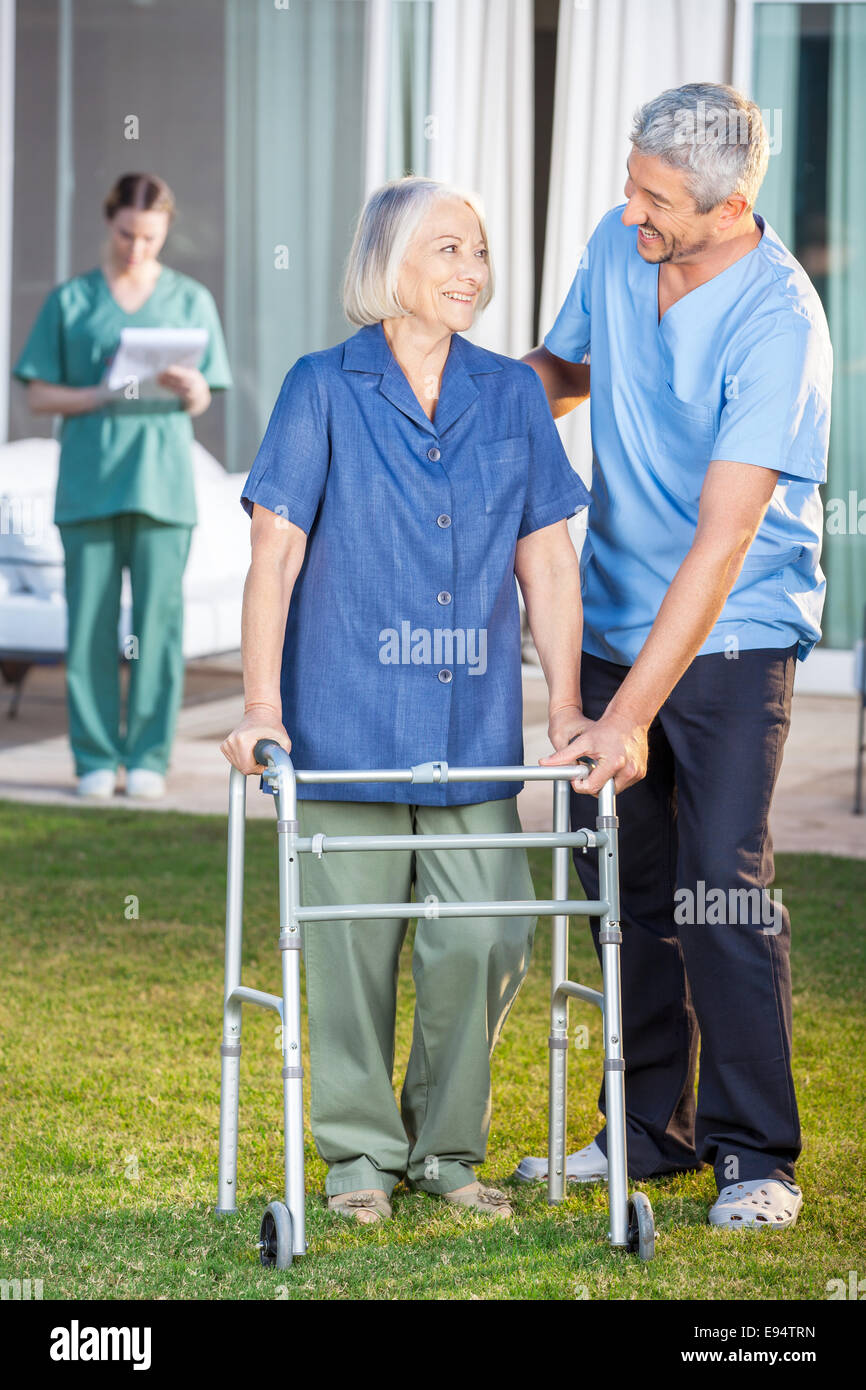 Caretaker Helping Senior Woman To Use Walking Frame Stock Photo