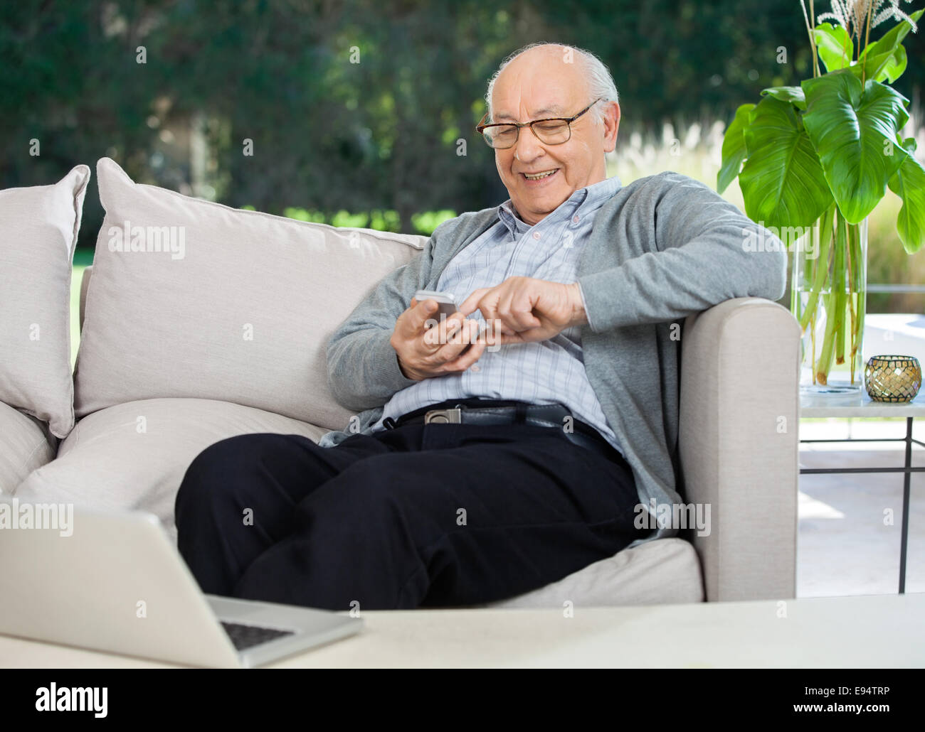 Happy Senior Man Text Messaging Through Smartphone At Porch Stock Photo