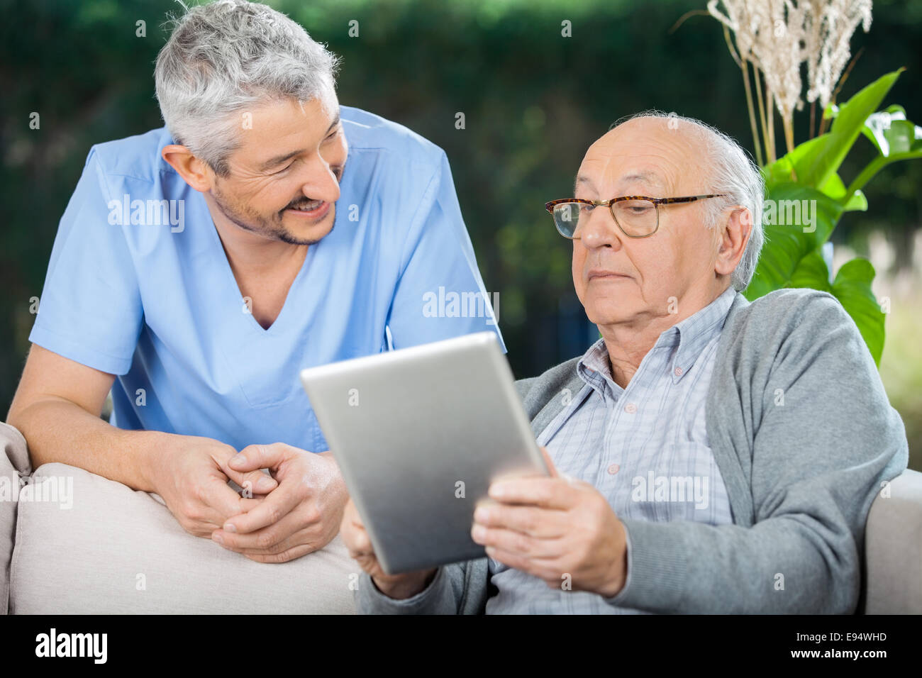 Male Caretaker Looking At Senior Man Using Tablet Computer Stock Photo