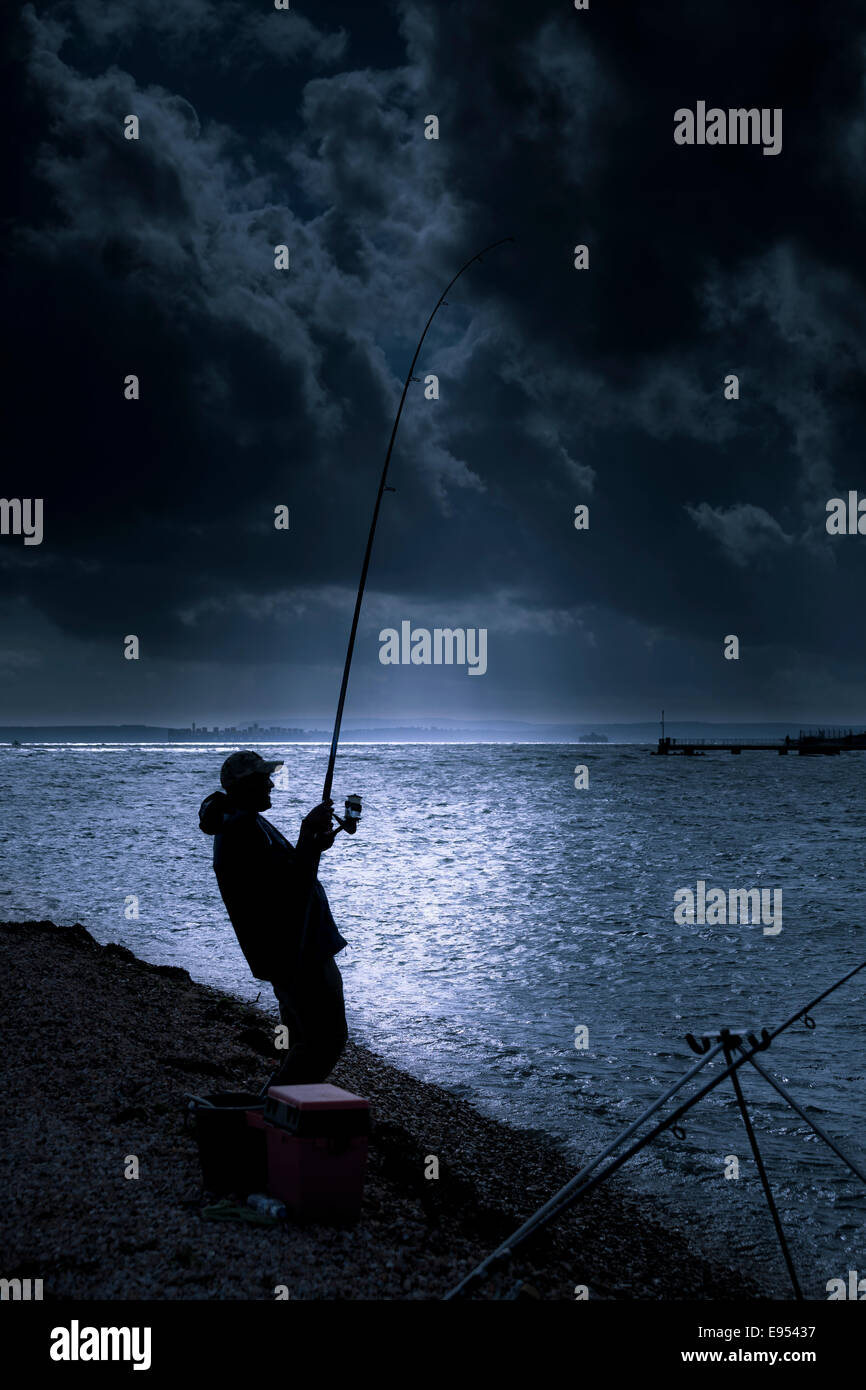 Semi silhouette of beach fisherman with rod bending from reeling in his catch. Stock Photo
