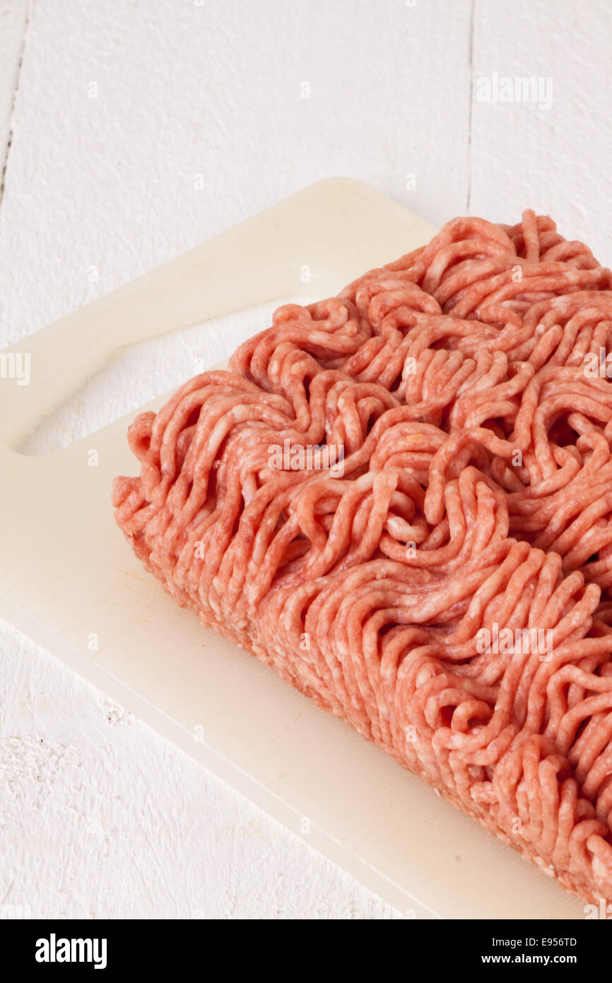 Block of unwrapped raw commercial beef mince from a store showing the texture and pattern of the mincer standing on a white plastic chopping board ready to be used in cooking Stock Photo