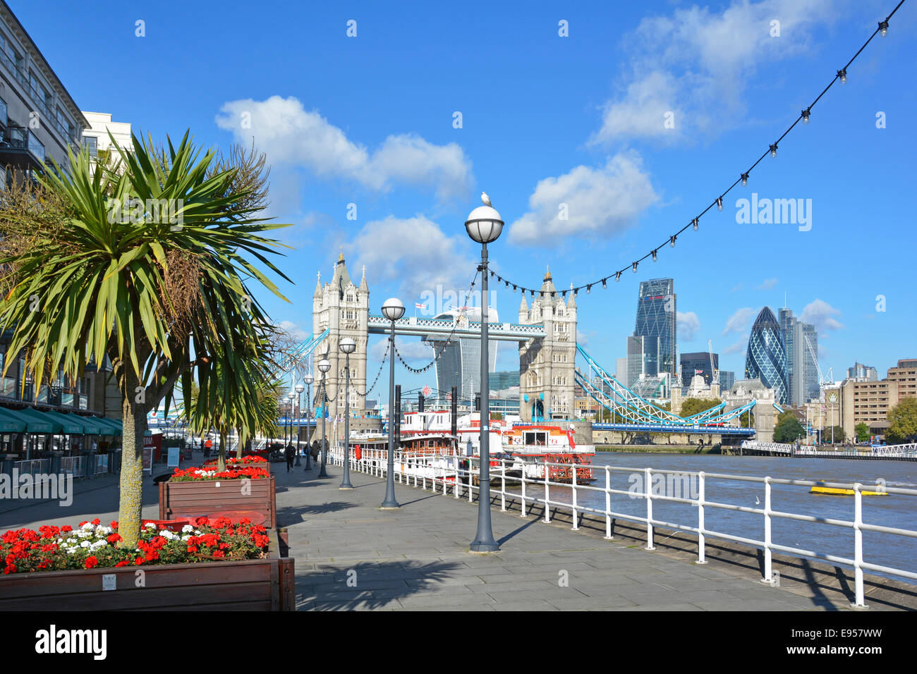 Thames Path Butlers Wharf on River Thames Tower Bridge views riverside apartments restaurants canopies & red flower cordyline tree planters London UK Stock Photo