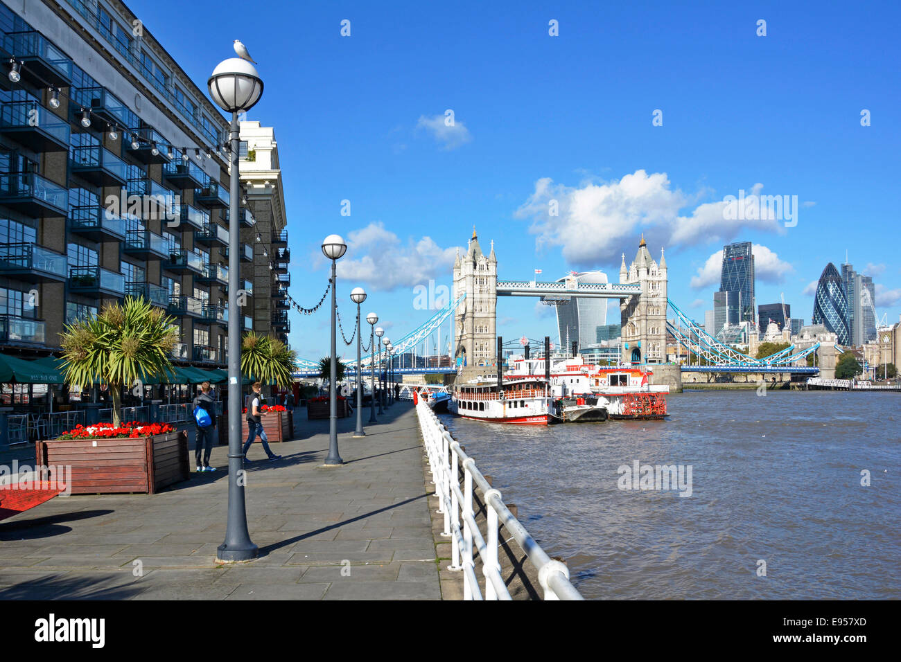 Butlers Wharf riverside walkway with skyline views of Tower Bridge and the modern skyscraper tower blocks of the City of London  flowers planters Stock Photo