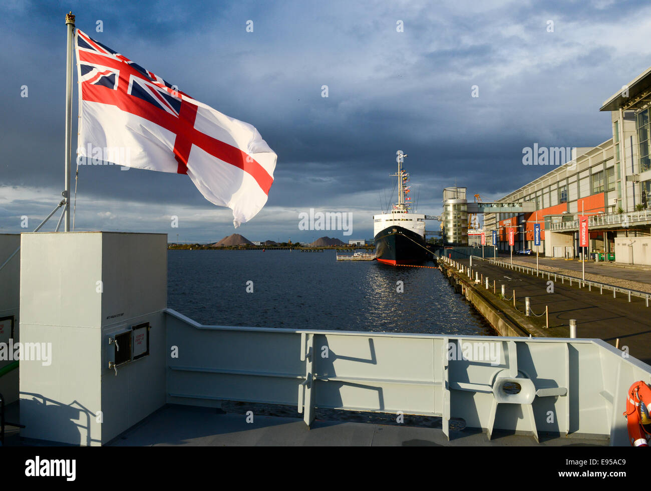 The White Ensign flying from HMS Tyne with the Royal Yacht Britannia at Ocean Terminal in Edinburgh Stock Photo