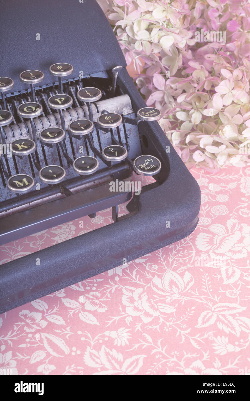 Close up of a vintage typewriter with floral pink table cloth and flowers. Stock Photo