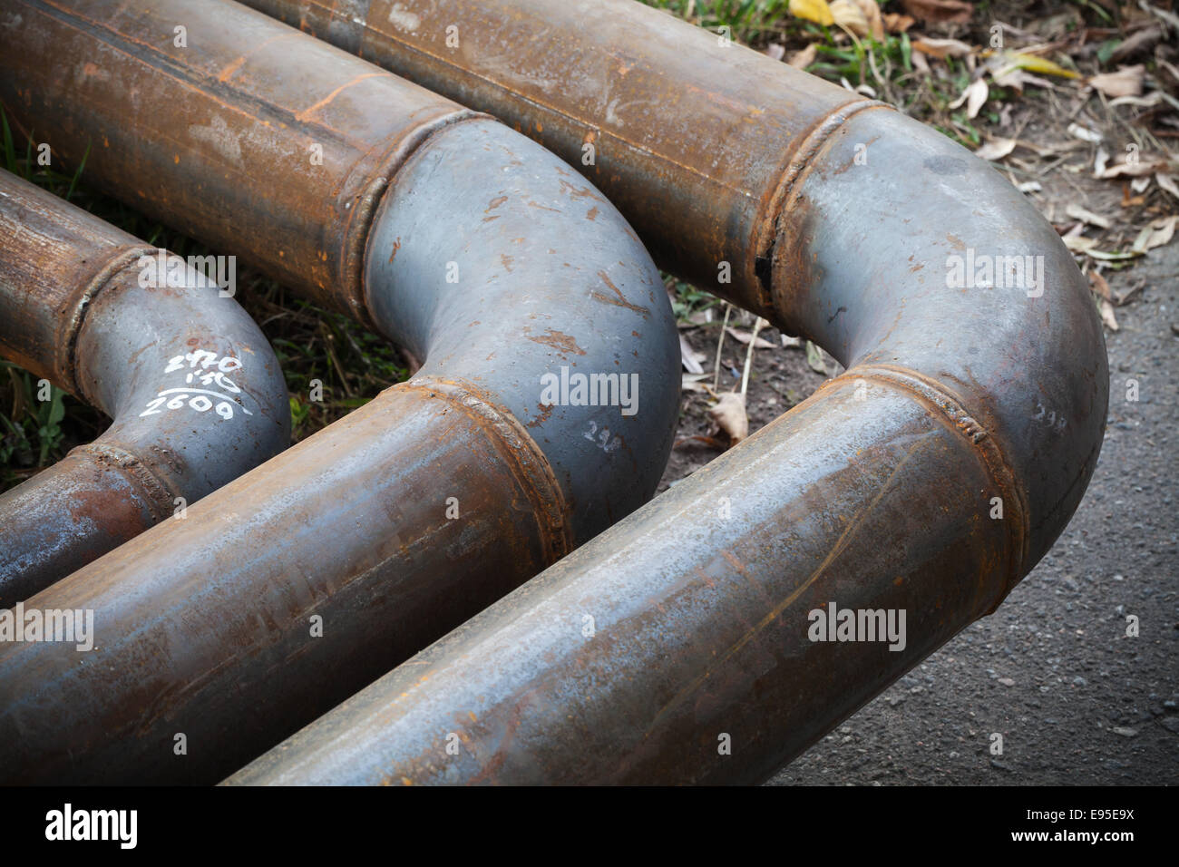 Bend of industrial steel pipeline over asphalt urban road Stock Photo