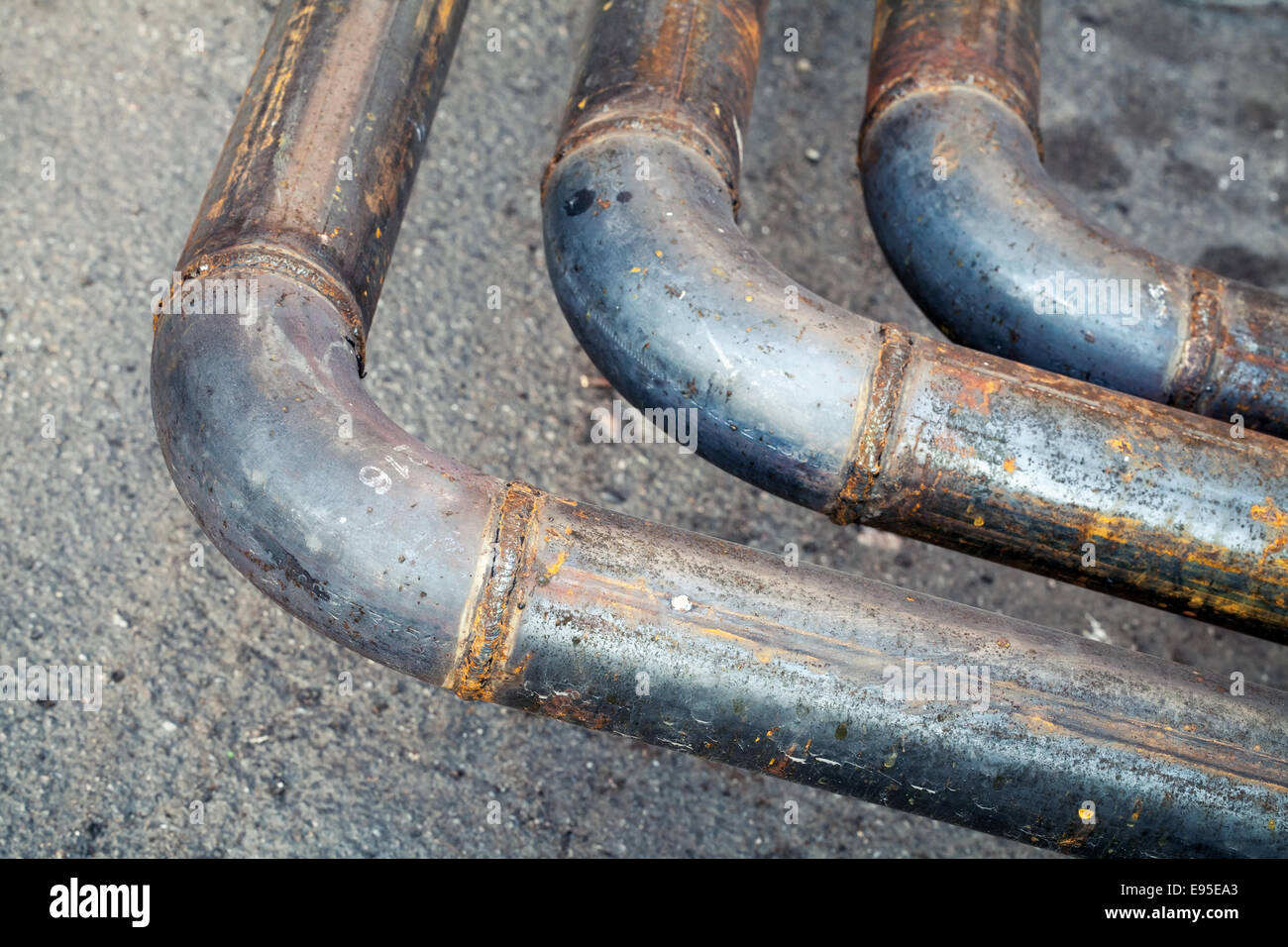 Bend of industrial outdoor steel pipeline over asphalt urban road Stock Photo