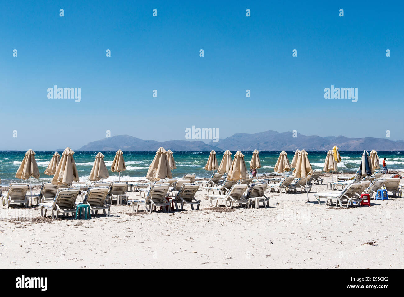 Empty beach with closed parasols and sun loungers on the beach of Mastichari, island of Kos, Greece Stock Photo