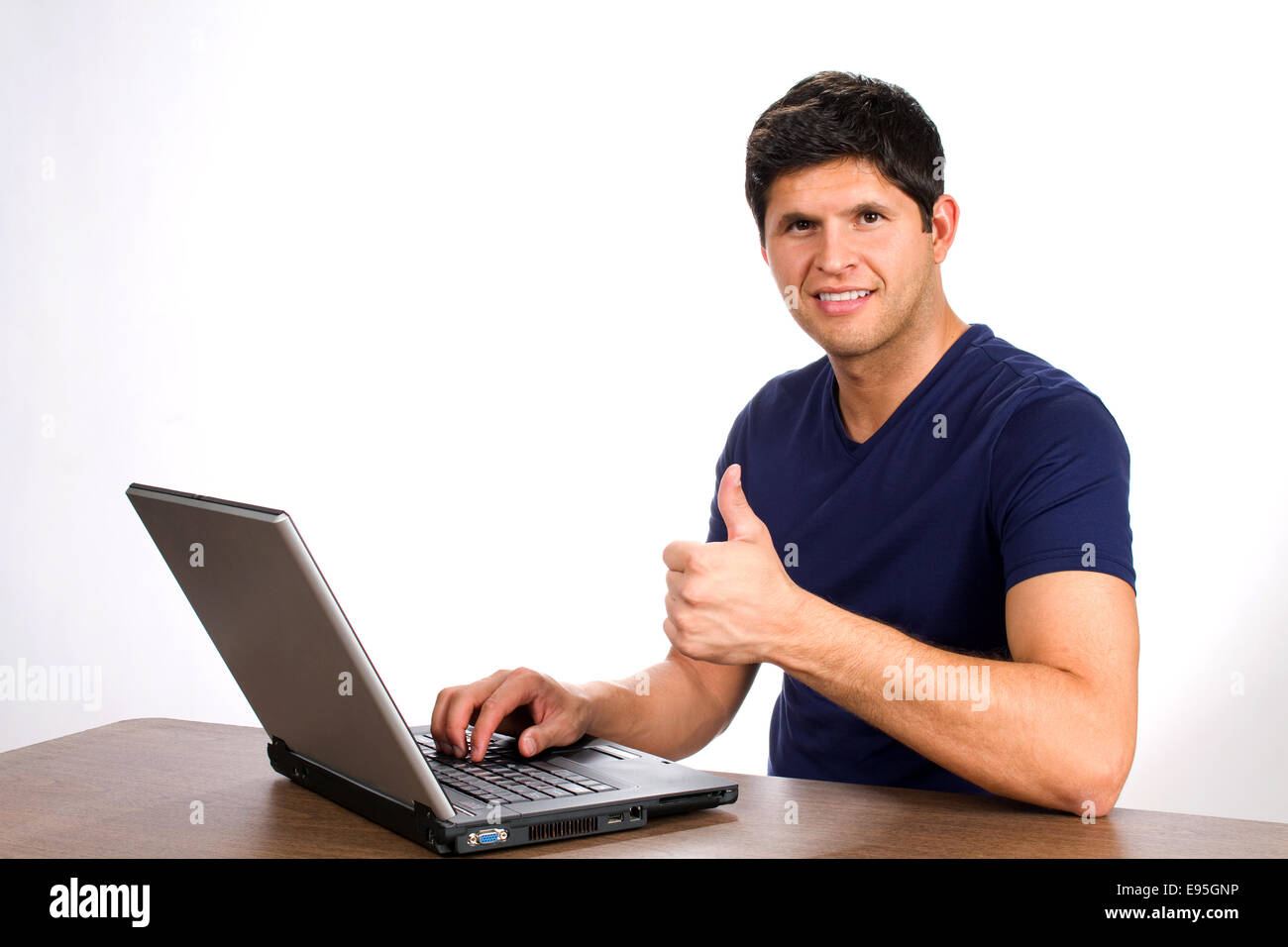 Young man smiles and gives a thumbs up sign after executing a successful internet transaction or purchase on a website from his Stock Photo