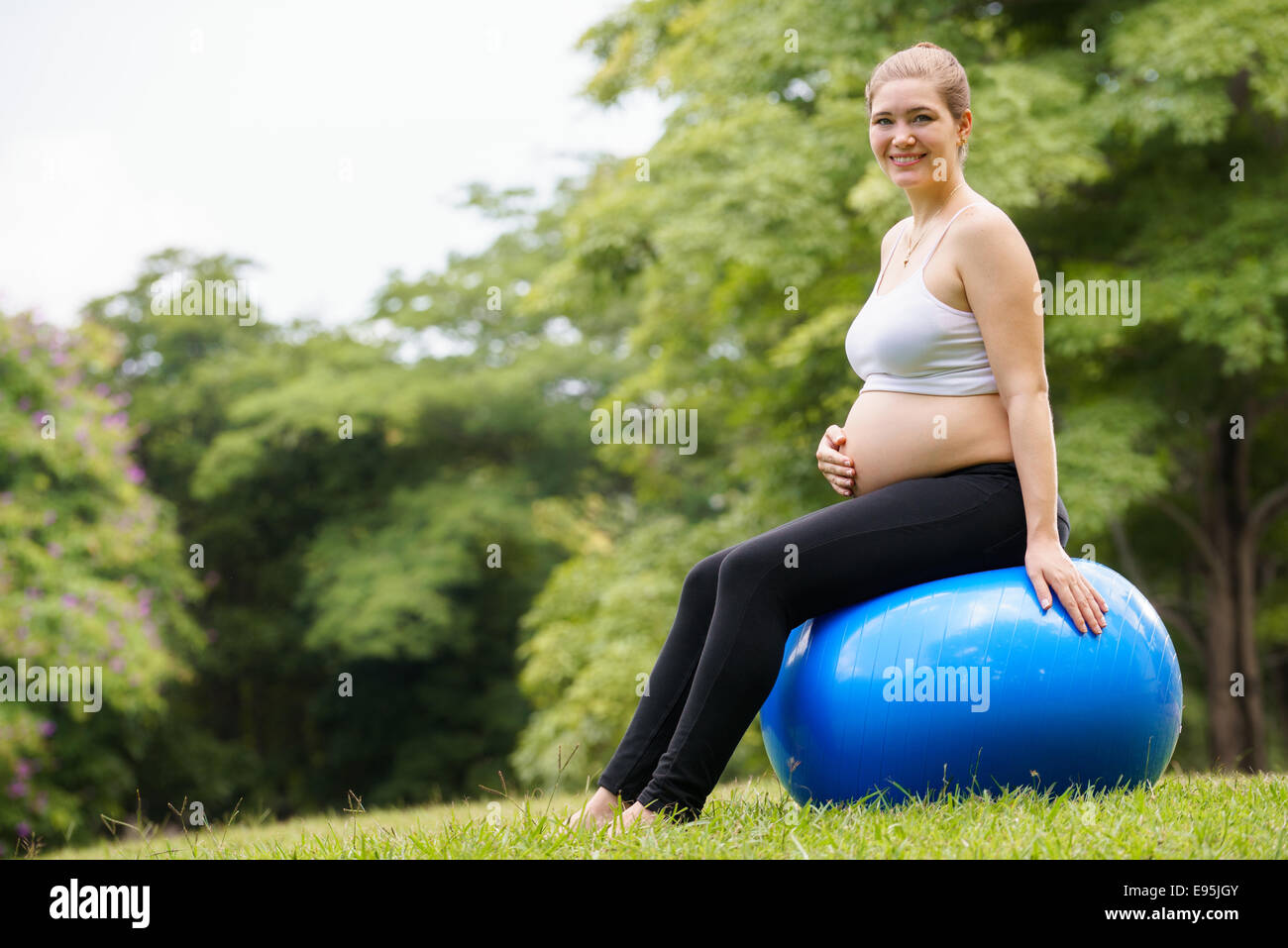 Portrait of white beautiful pregnant woman doing fitness exercise in park training back muscles on fitness ball. Copy space Stock Photo