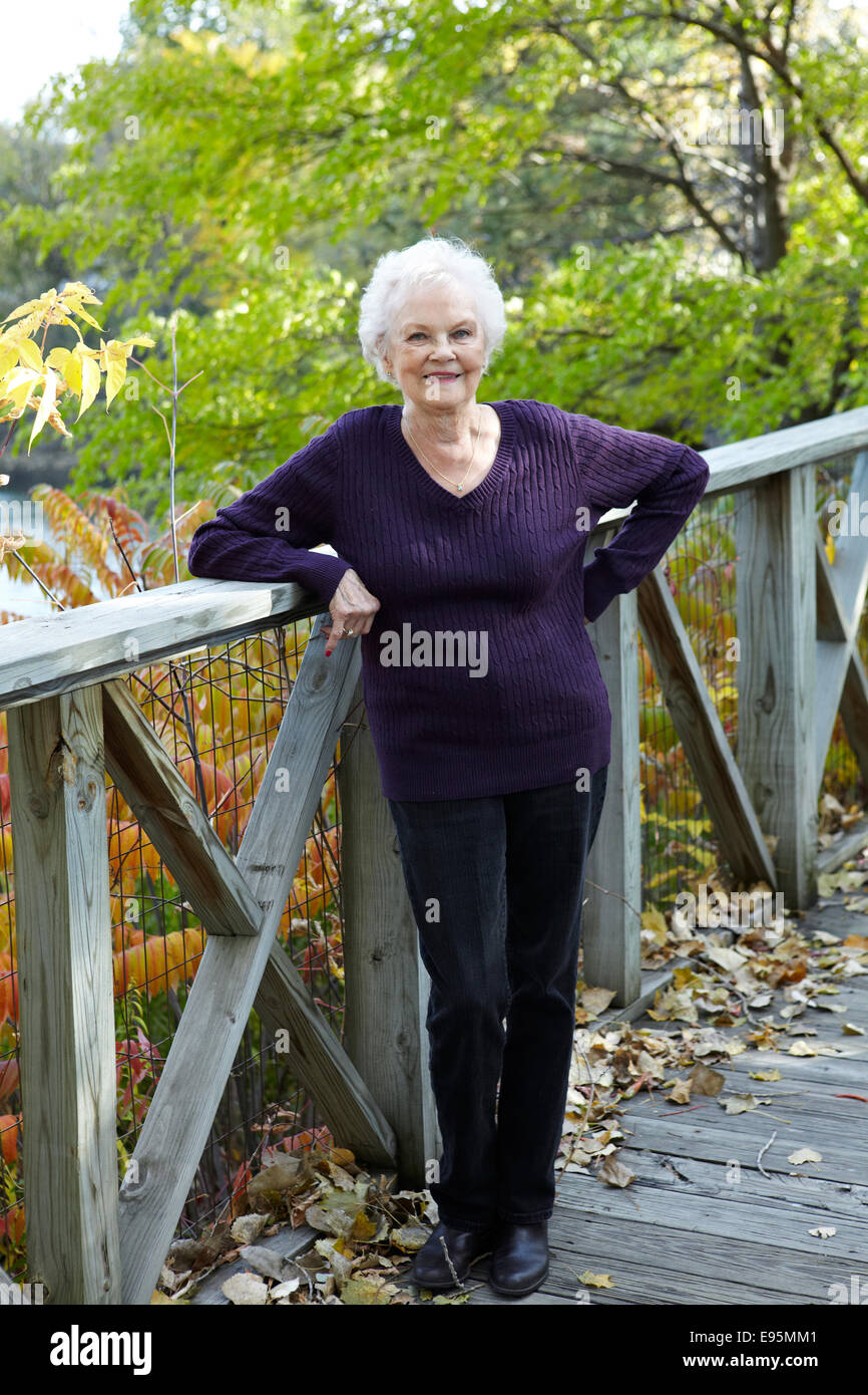 85 year old woman standing on dock ramp in Autumn landscape. Stock Photo