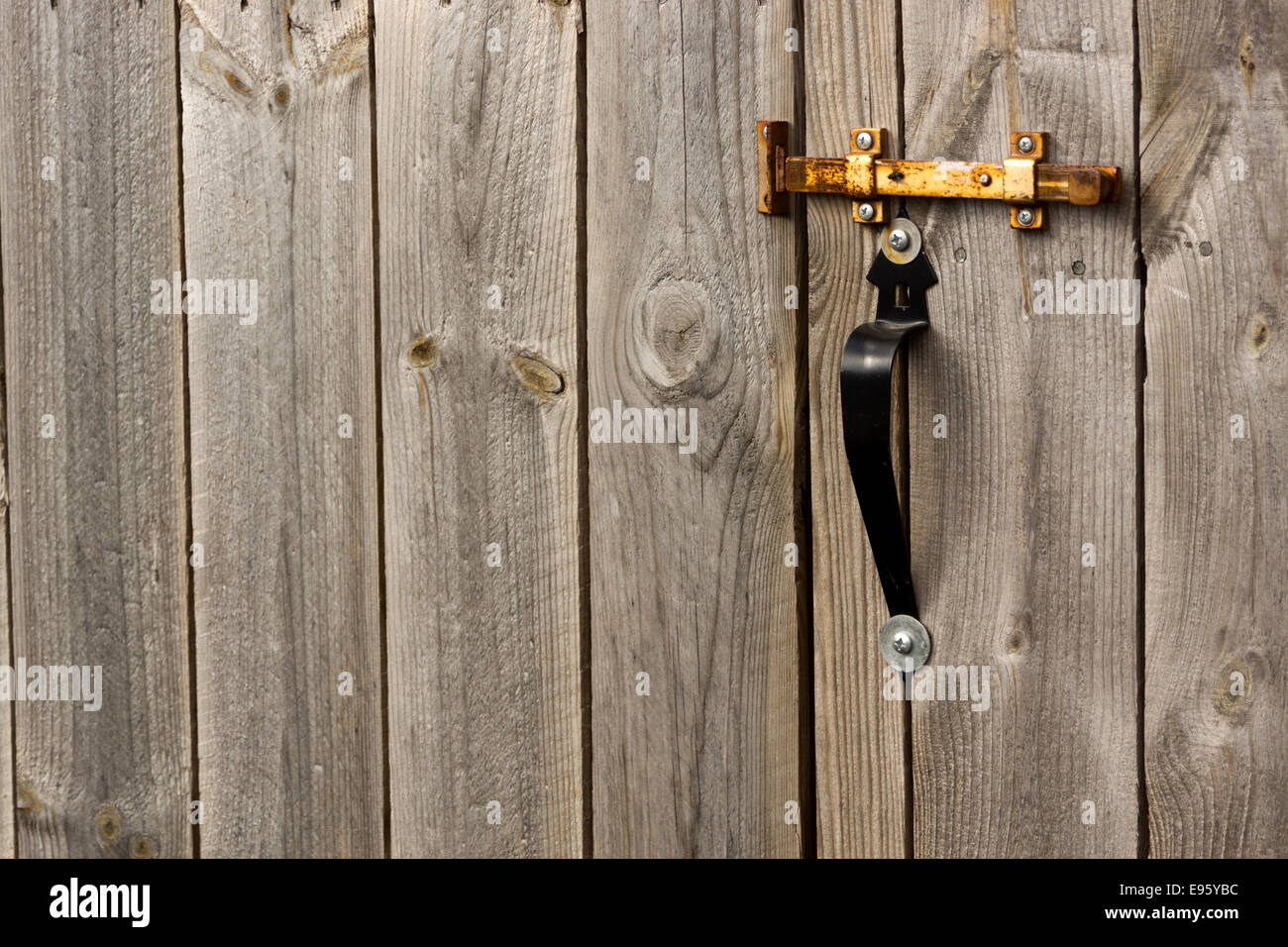 Rusty latch on a door through a plank fence. Stock Photo