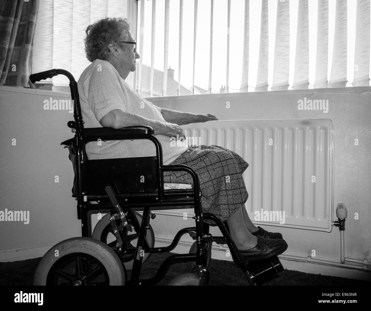 Ninety year old woman with hand on radiator looking out of window. UK. Coronavirus, self isolation, social distancing, quarantine... concept Stock Photo