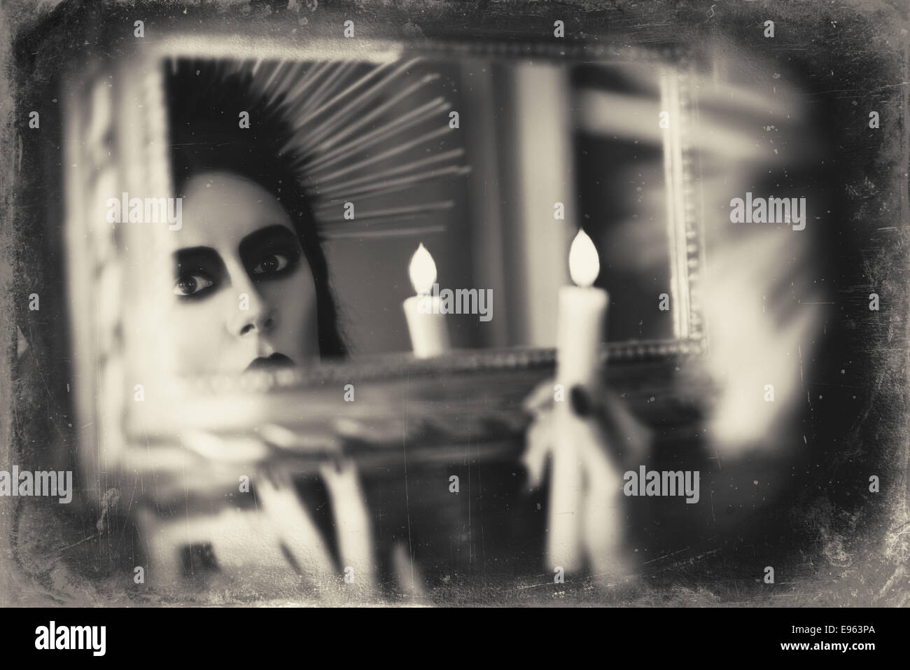 Beautiful goth girl holding candle in hand and looking into the mirror. Grunge texture effect Stock Photo