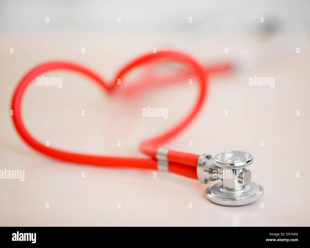 Red medical stethoscope in shape of heart on table Stock Photo