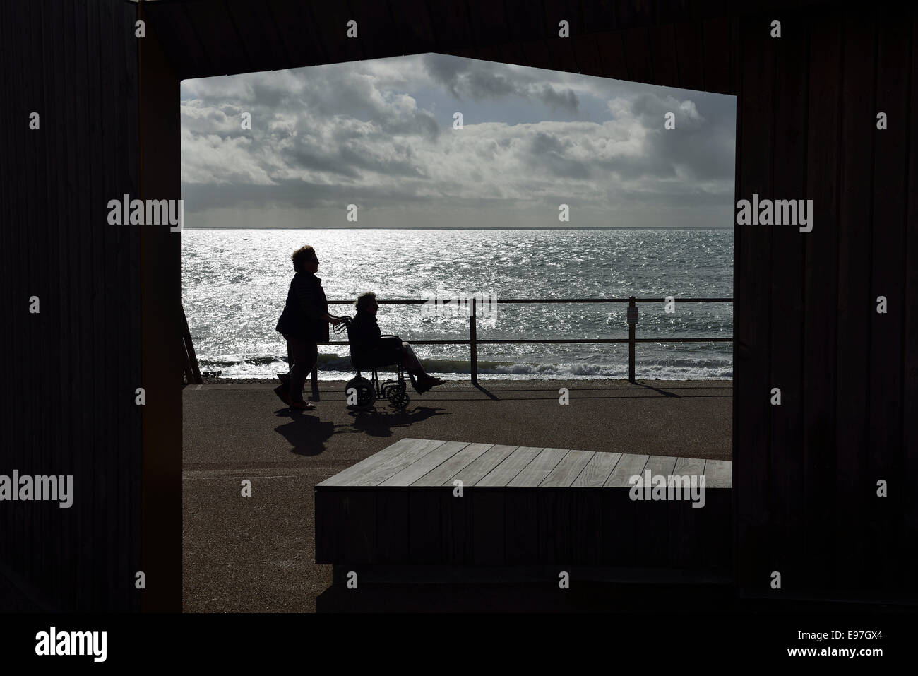 A woman pushing a mature woman in a wheelchair along Bexhill on Sea promenade. Stock Photo