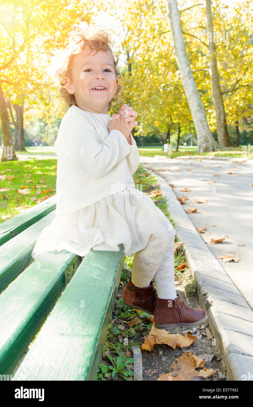 Happy little girl sitting on bench in the park Stock Photo - Alamy