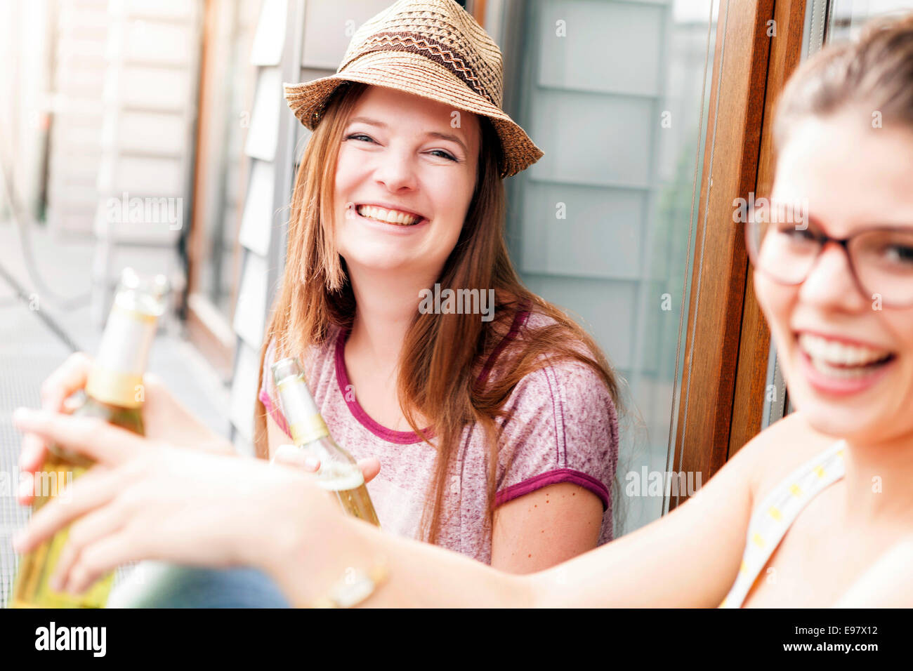 Two young women drinking beer on balcony, Munich, Bavaria, Germany Stock Photo
