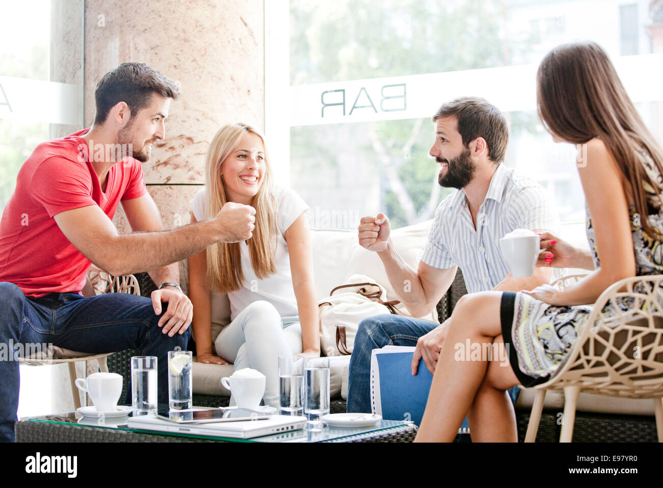 Male students in cafe preparing for fist bump, girlfriends watching Stock Photo