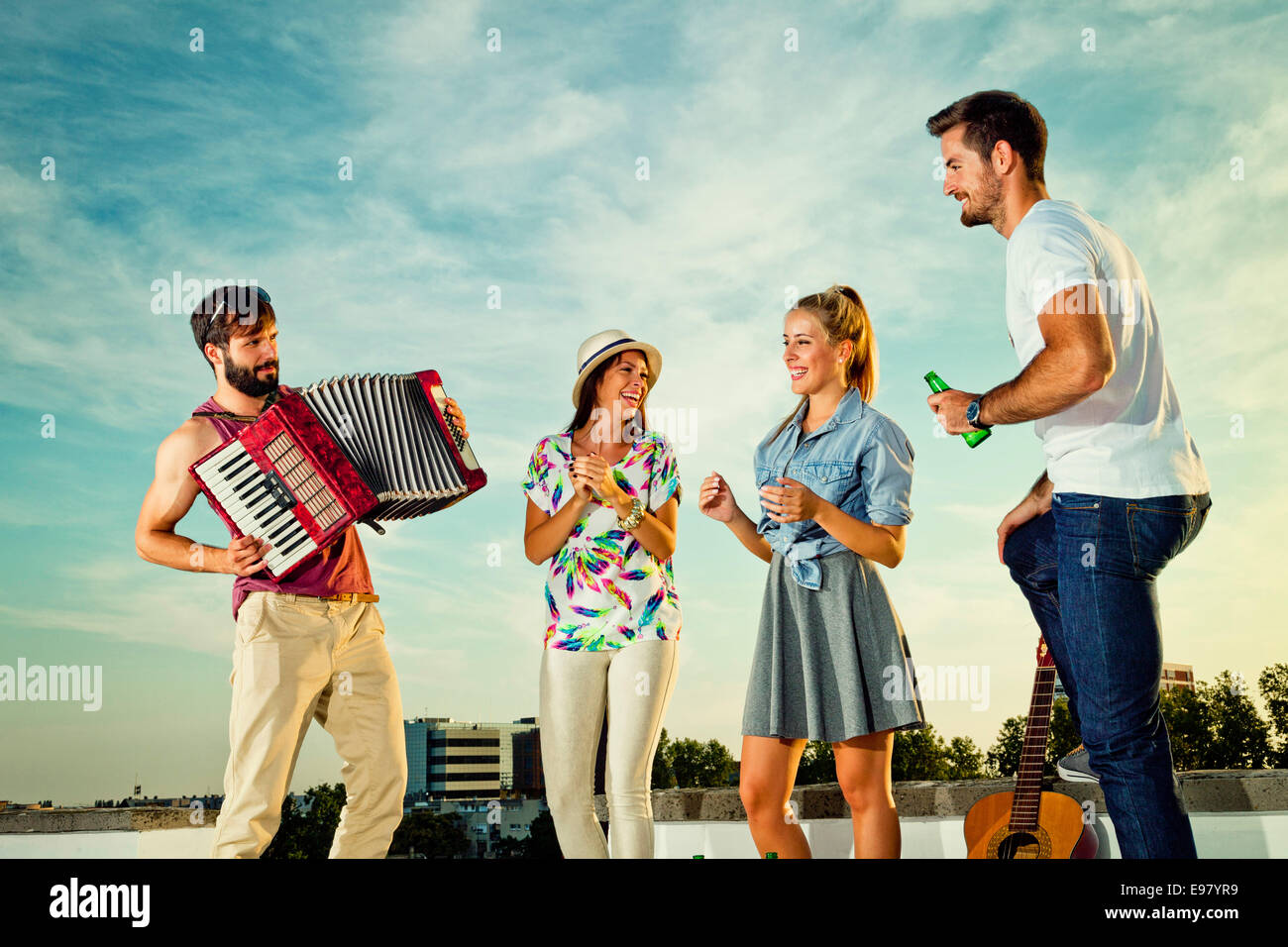 Man playing accordion while friends dancing at rooftop party Stock Photo