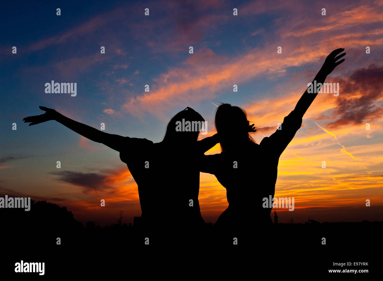 Young women with arms raised dancing at sunset Stock Photo