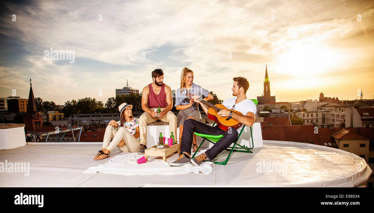 Young people listening to guitar music at rooftop party Stock Photo