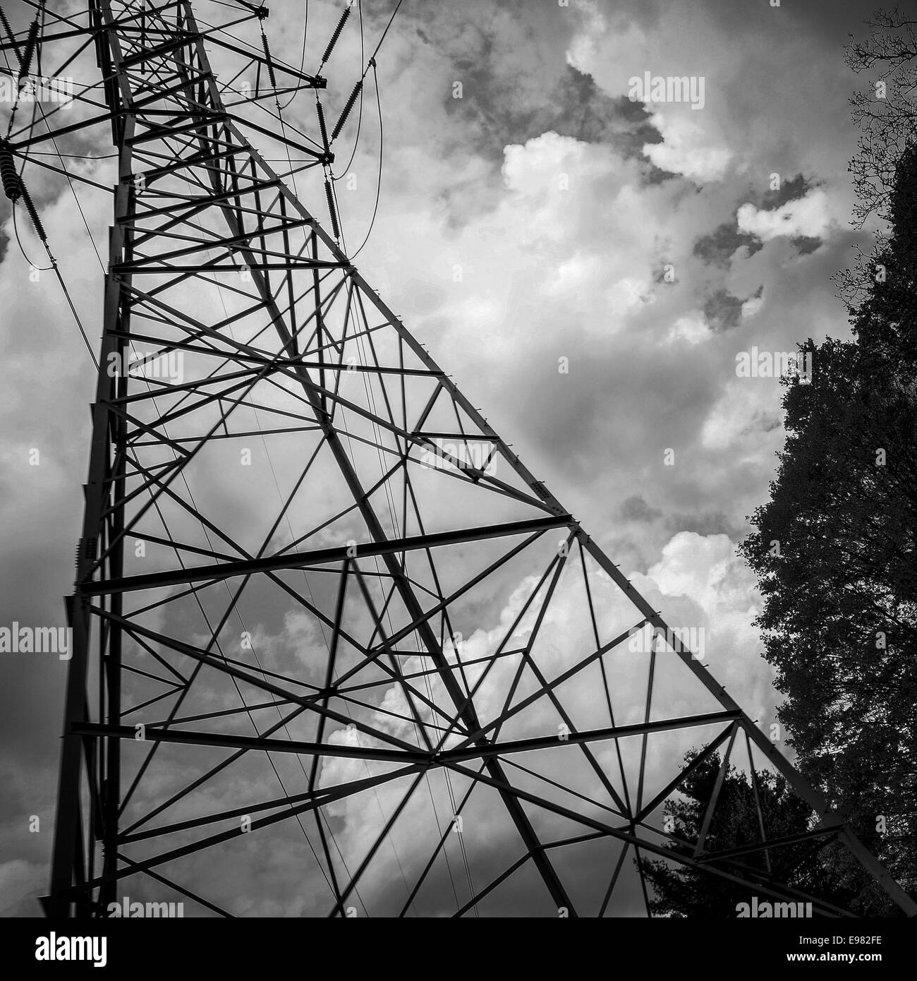 Black and White low angle view of metal electric tower against intense storm clouds. Stock Photo