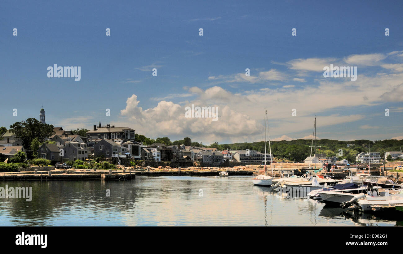 View bay waterway in center reflecting sky seaside buildings on left recreational sailboats on right. Green hills trees in Stock Photo