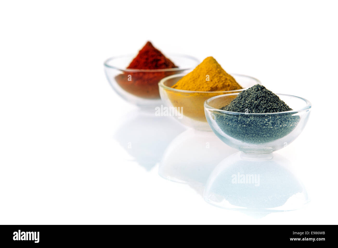 Neat conical heaps of black lava salt, curry and chilli or red pepper powder in clear transparent glass bowls on a white background with reflection and copyspace Stock Photo