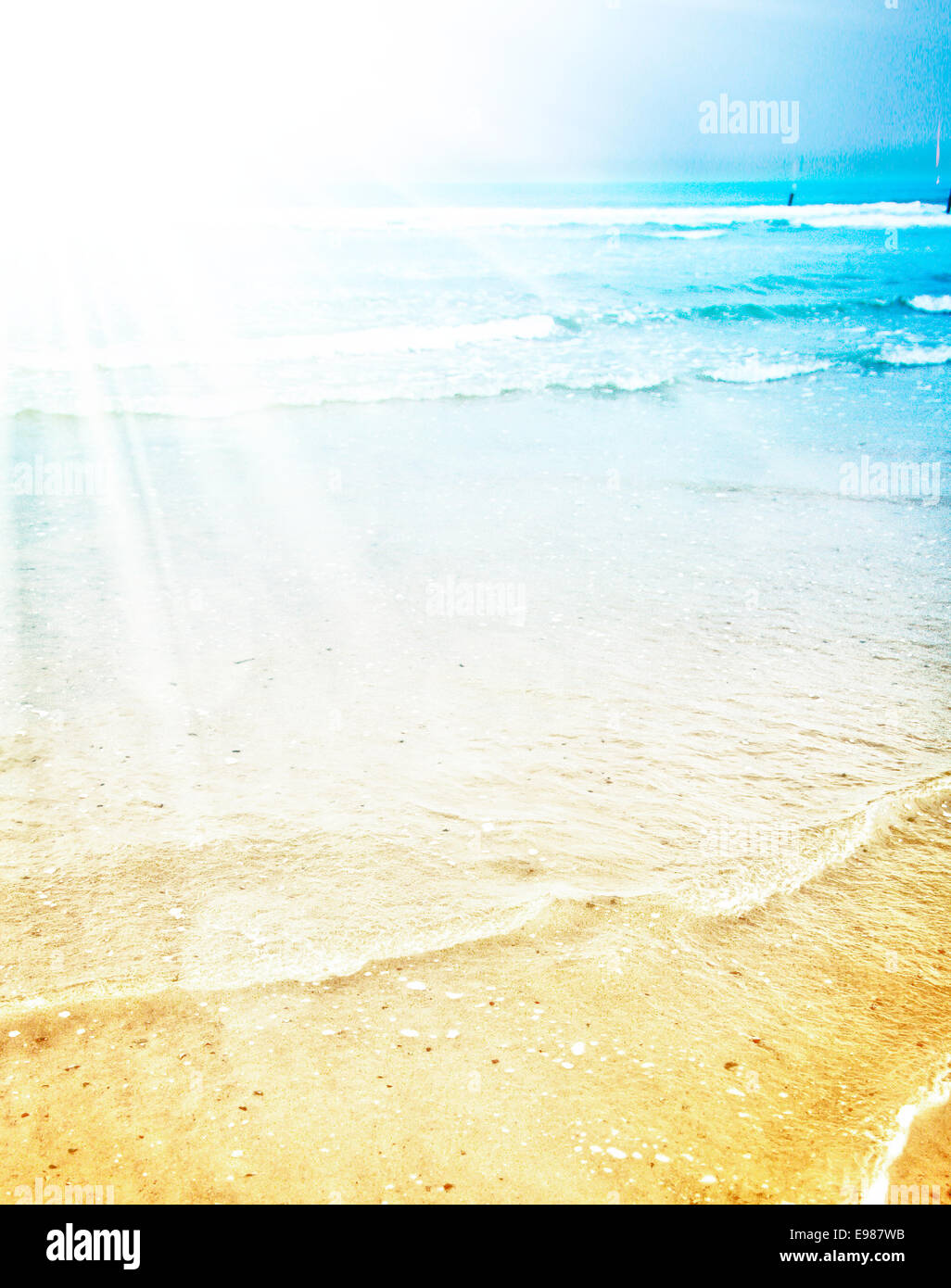 Bright summer sunshine on a tropical beach with the sun's rays radiating across the turquoise blue water and empty sand Stock Photo