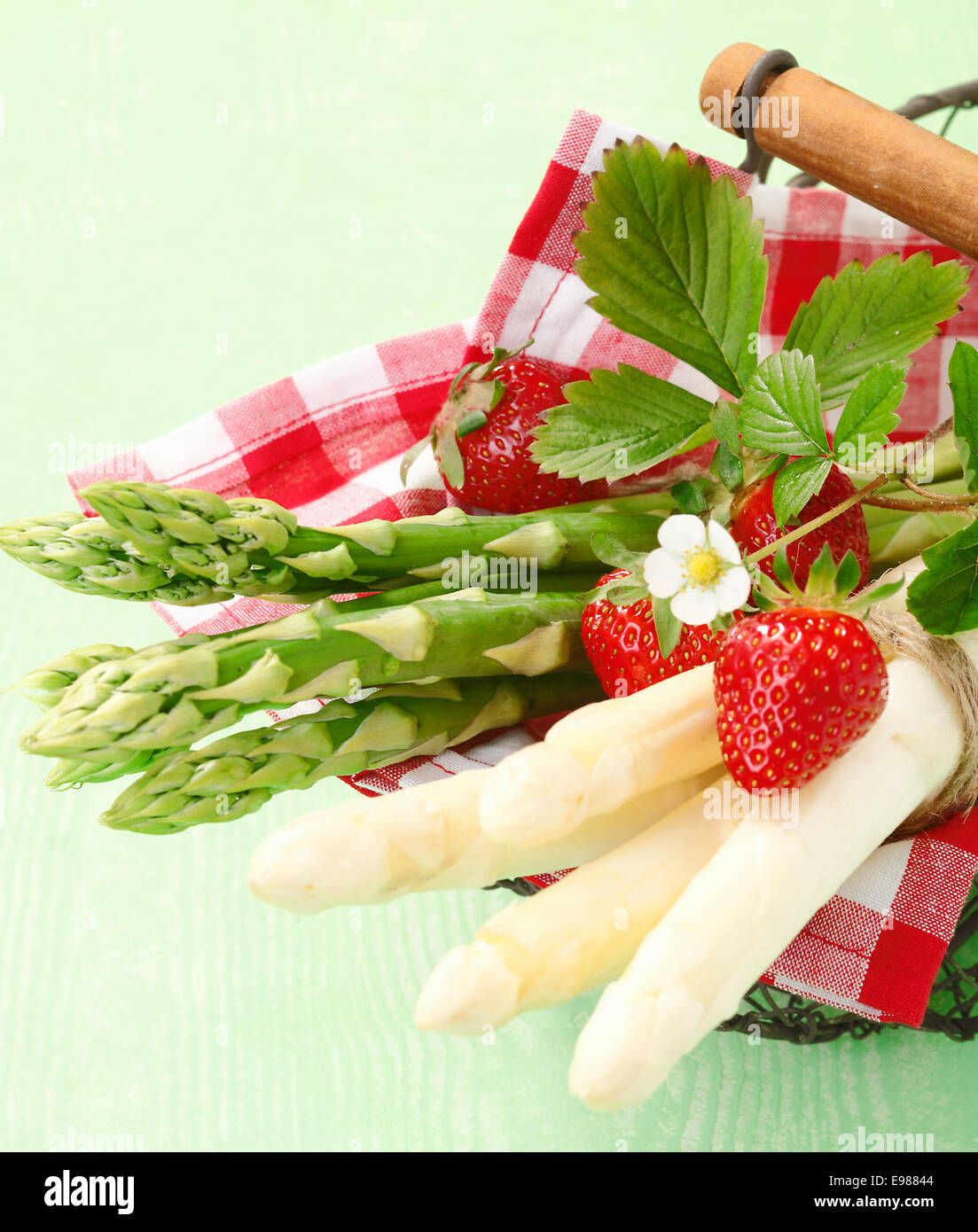 Serving of fresh green and white asparagus tips on a cheerful red and white checked napkin with strawberries Stock Photo