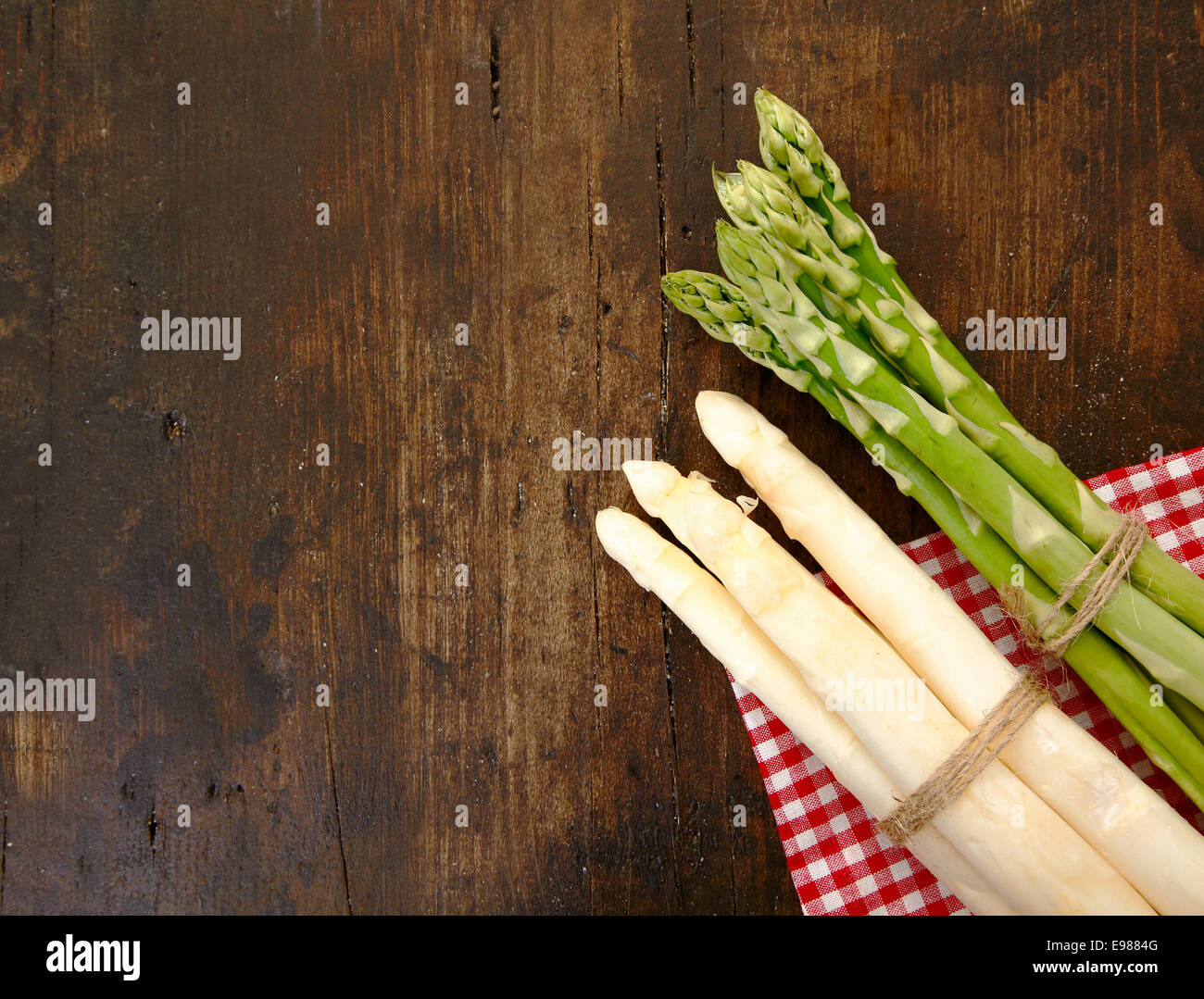 Fresh bunches of green and white asparagus lying on a checked napkin on a textured wooden surface with copyspace Stock Photo