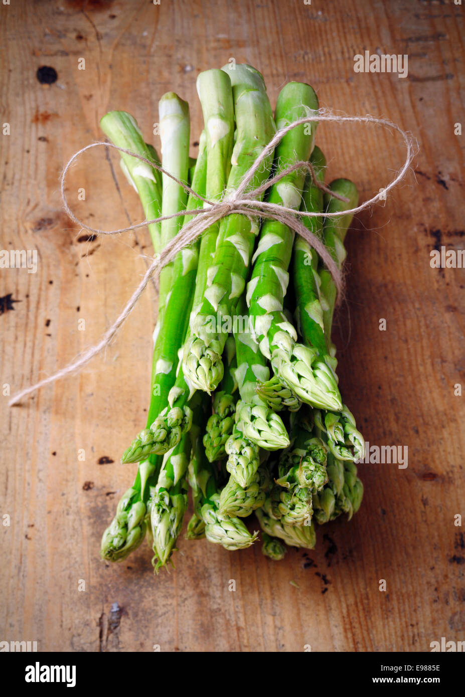 Bunch of fresh green asparagus spears tied with a bow on a rustic wooden table top Stock Photo