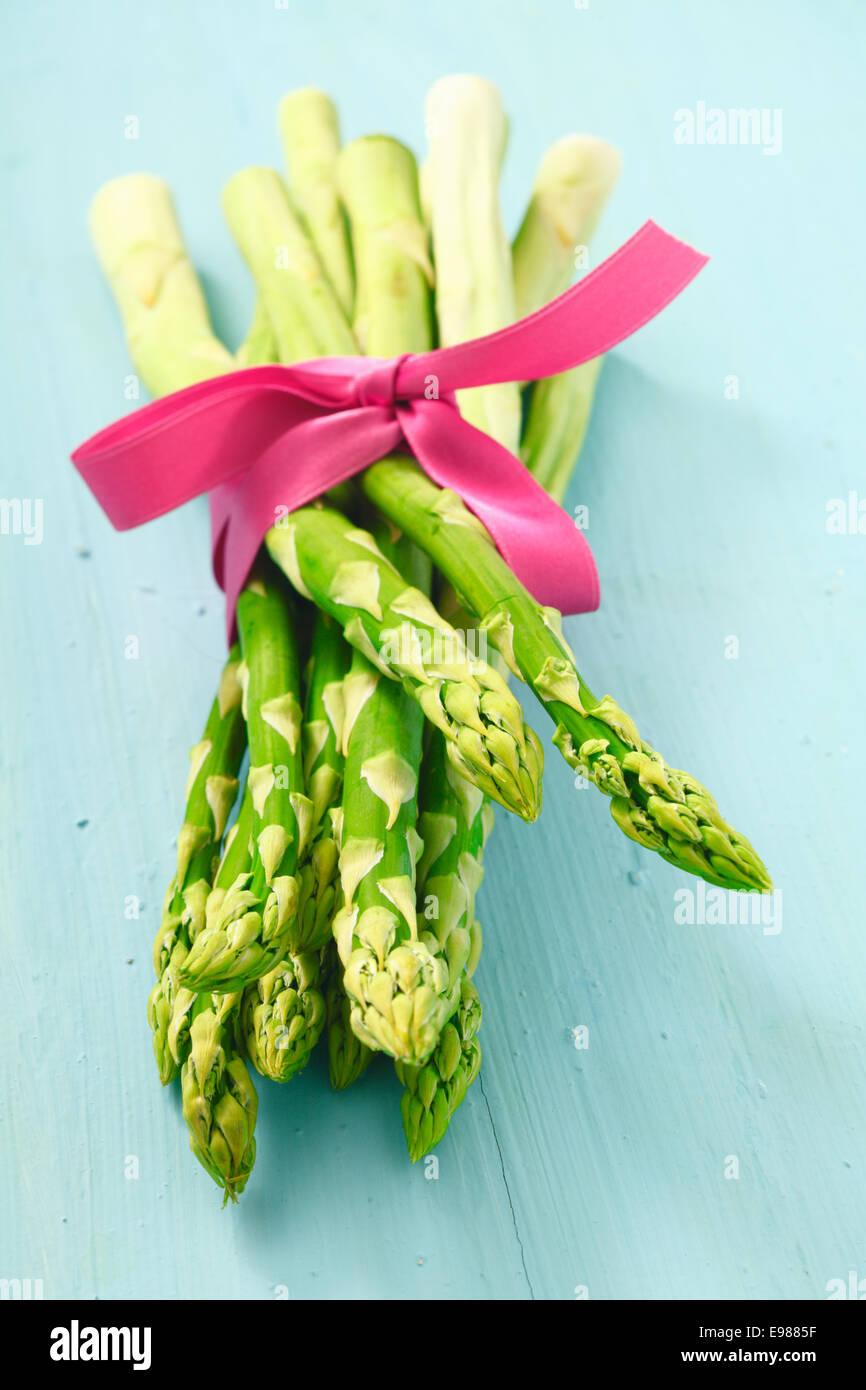 Bunch of fresh young asparagus tips tied with a decorative pink ribbon pointing towards the camera Stock Photo