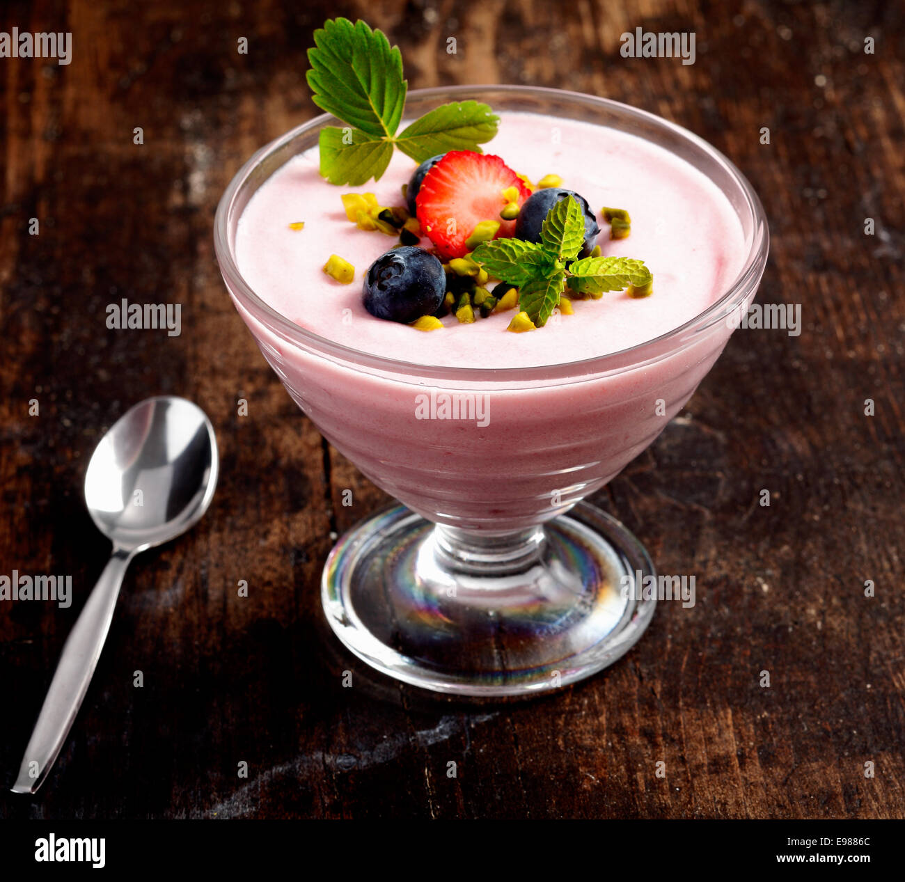 Sweet dessert of strawberry cream. Topped with some blueberries and a leaf of mint. Standing on a rustic wooden background. Stock Photo