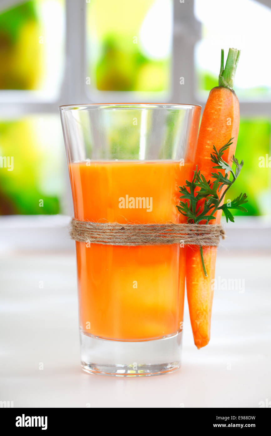 Delicious healthy liquidised carrot juice in a tall glass with a fresh whole carrot tied to the side with string Stock Photo