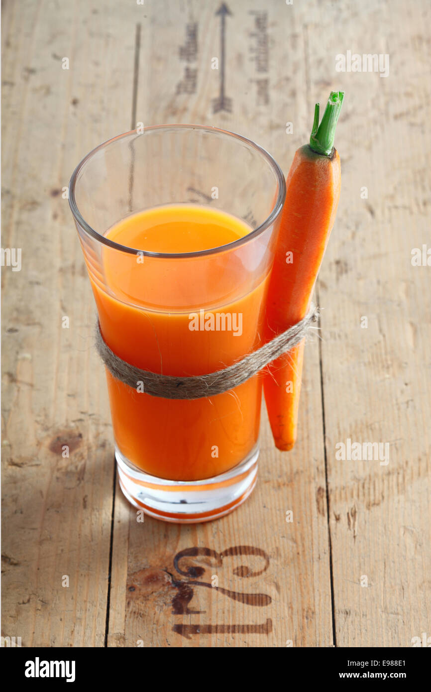 Fresh vegetarian carrot juice blend in a tall glass on an old wooden surface with stamped numbers with a whole carrot tied to the side Stock Photo