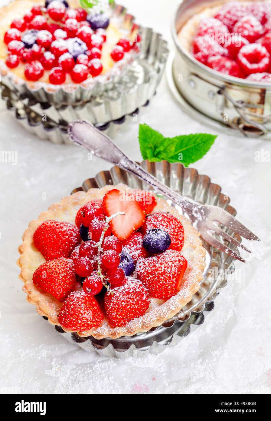 Gourmet fresh fruit mixed berry tartlets on crisp golden pie crusts served in individual decorative fluted metal pie pans Stock Photo