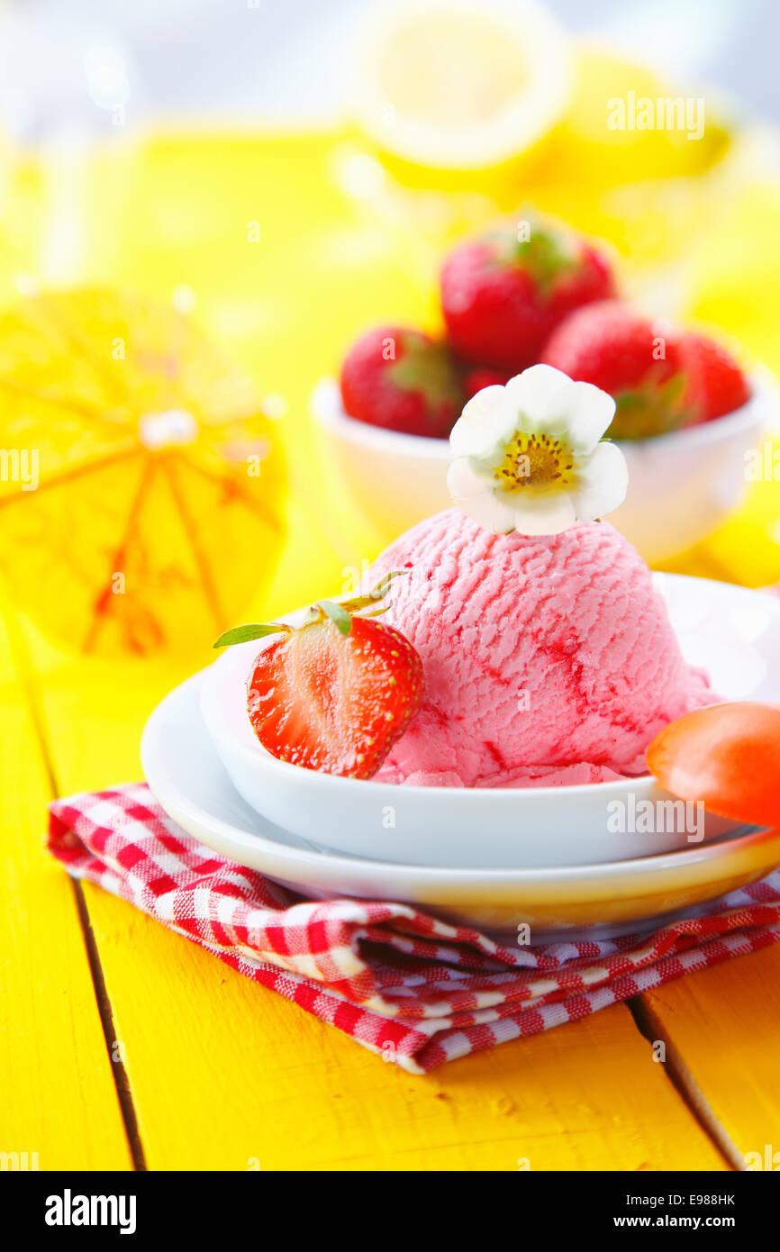 Enjoying a serving of fresh strawberry icecream on a yellow tabletop poolside in summer Stock Photo