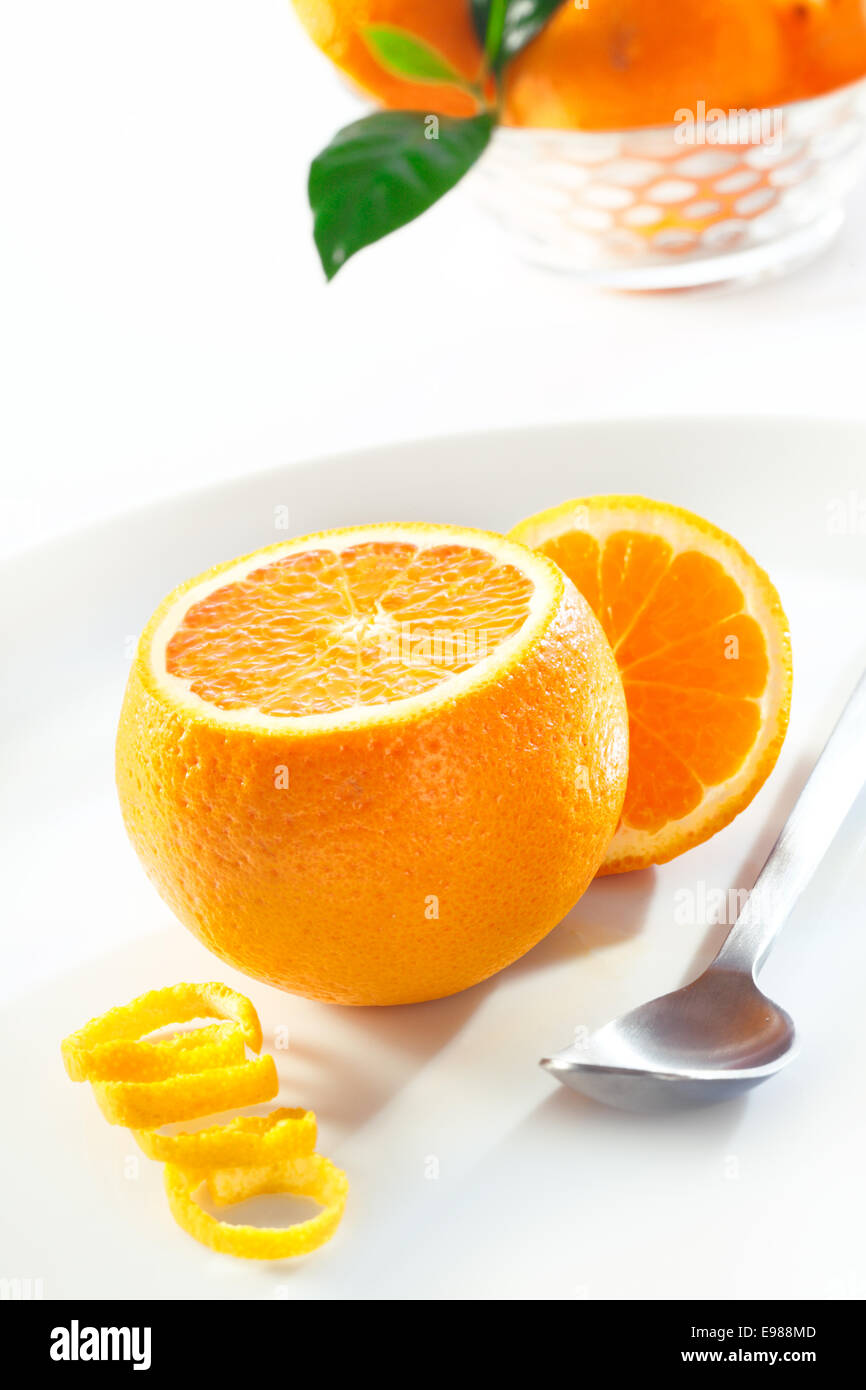 Fresh juicy orange with the top cut off to display the succulent pulp served with a spoon and colied zest Stock Photo