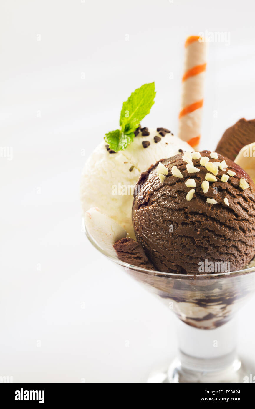 Balls of chocolate and vanilla ice-cream topped with chopped nuts in a conical glass parfait dish Stock Photo