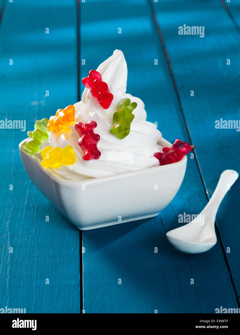 Funny Frozen Yogurt with gummi bears as topping on a wooden blue background Stock Photo