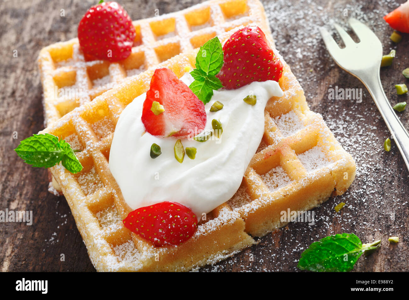 Closeup of a dollop of fresh whipped cream and sliced fresh strawberries topping a crisp golden waffle Stock Photo