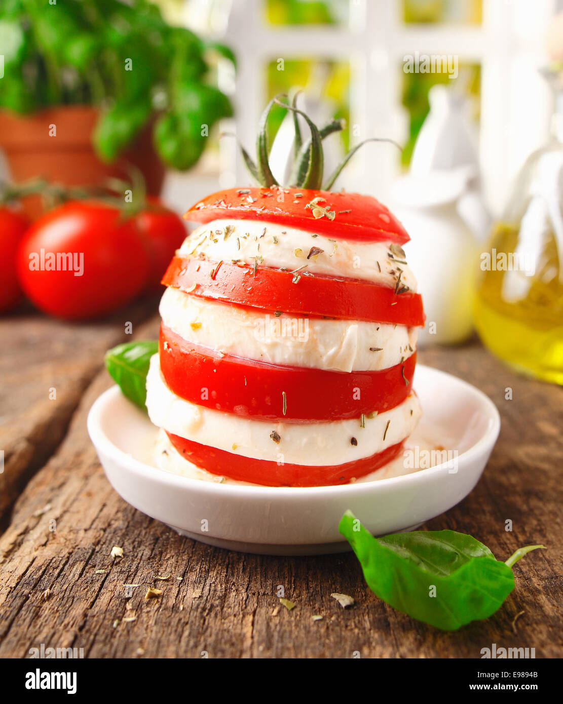 Preparing an individual gourmet cheese and tomato salad with a tower formed of alterning slices standing on a rustic wooden kitchen table Stock Photo