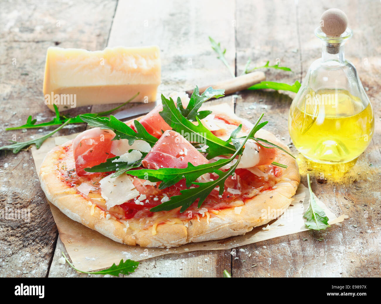 Preparing homemade ham pizza with fresh ingredients including thinly sliced ham, cheese, herbs and tomato Stock Photo